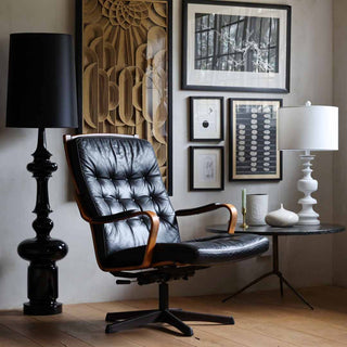 An image of a living room with art on the walls, a leather swivel chair, a table lamp and black floor lamp