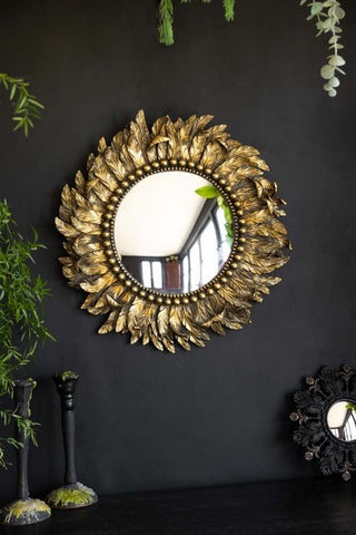 A gold feathered effect framed circular mirror against a black wall.