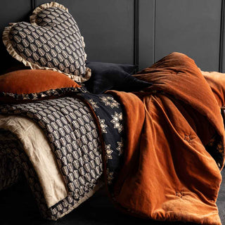 A gorgeous burnt orange velvet throw styled on a bench and layered with a black and natural block printed fern pattern throw and matching heart ruffle cushions. 