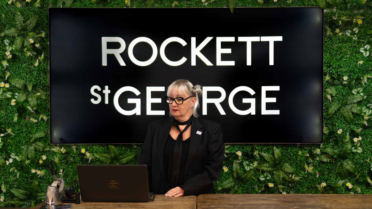 A green living wall with a black and white Rockett St George logo and a woman at a till.