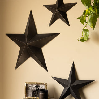 The Set Of 3 Black Metal Stars displayed on/leaning against a neutral wall, styled with a plant, photo frame and candle. 