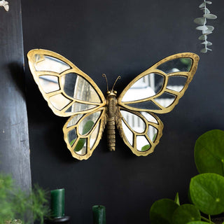 A pink and red playing card style mirror styled with a crystal and a candlestick holder, in front of a black background with some greenery and another mirror.