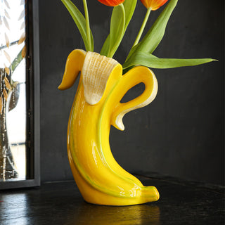 The Banana Vase with tulips inside, displayed on a black sideboard in front of a mirror.