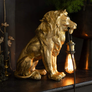 A gold lion lamp styled on a black surface with some accessories and some greenery.