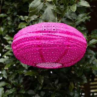 A hot pink outdoor lantern hanging from a tree.