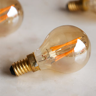 Lifestyle image of Golf Ball E14 4W Amber LED Light Bulbs arranged on a white marble surface. 