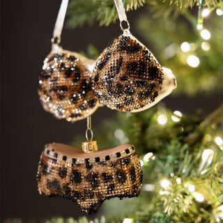 The Shit Happens Christmas Tree Decoration hanging in front of a black background with fairy lights.