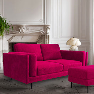 The Large Grace Sofa in Harry's Pink, styled in a living room with the matching footstool, a table lamp and a plant.