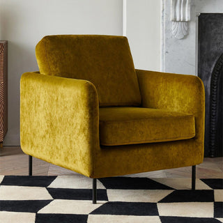 The Edie Needlecord Velvet Green Armchair styled on a geometric rug in a living room.