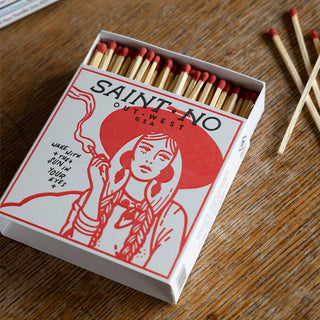 Lifestyle image of the Out West Luxury Matches by Saint No displayed open with several loose matches laid out on a wooden table. 