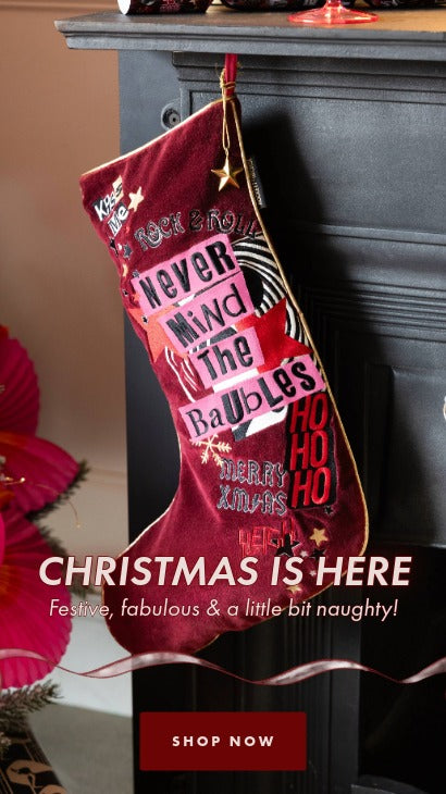 Red Christmas stocking with festive text hanging on a fireplace.