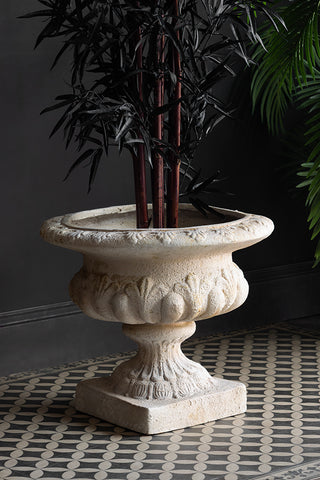 The Classical Stone-Effect Planter with a plant inside, styled on a geometric floor with another plant in the background.