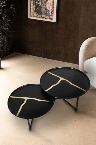 A nest of two black coffee tables with gold inlay styled on an oatmeal carpet next to an armchair