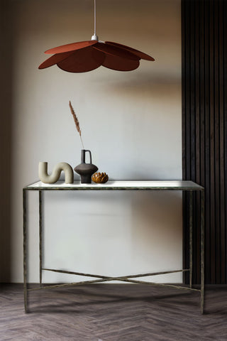 A console table made from metal and glass, styled with art deco-inspired ornaments below a rust-red ceiling light