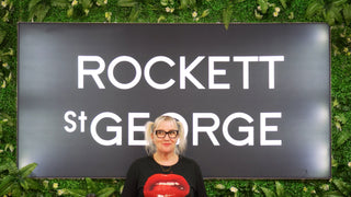 Image of the Rockett St George sign on a vertical garden wall. In front of the sign is Tina B, our Outlet and Ebay Store Supervisor