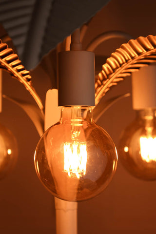 Lifestyle image of the Globe E27 6W Amber LED Light Bulb styled on a white lamp. 