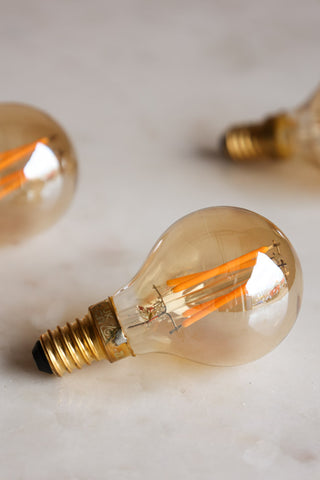 Lifestyle image of three Golf Ball E14 4W Amber LED Light Bulbs together on a white surface.