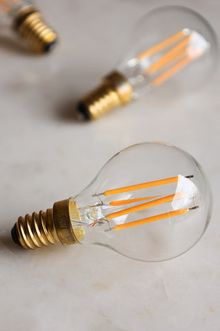 Lifestyle image of three Golf Ball E14 4W Clear LED Light Bulbs together on a white marble surface.