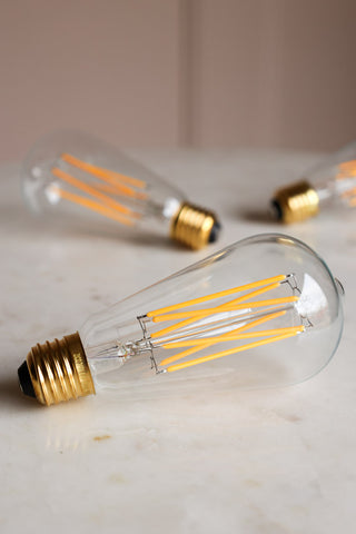 Lifestyle image of three Squirrel Cage E27 6W Clear LED Light Bulbs on a white marble surface.