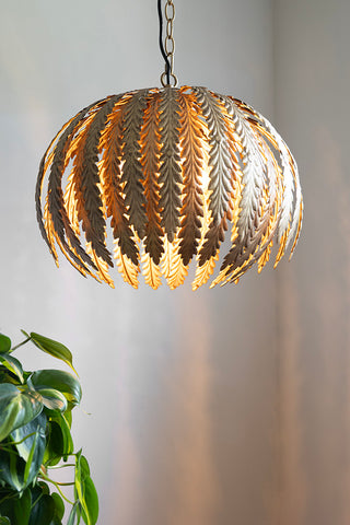 The Tropical Leaf Ceiling Pendant Light switched on and styled above a plant.