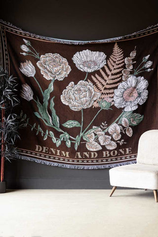 The Denim & Bone Scandi Black Woven Cotton Throw styled hanging on a dark wall next to a chair and a plant.