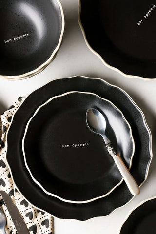 A styled image of the 12 Piece Black & Off-White Edge Bon Apetit Dinner Set with a spoon on one of them.