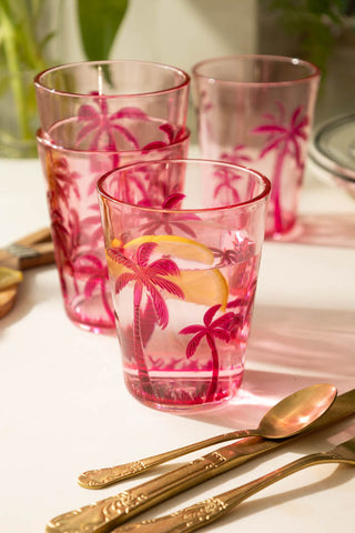 A lifestyle image of multiple acrylic pink palm tree tumbler glasses stacked up and around eachother.
