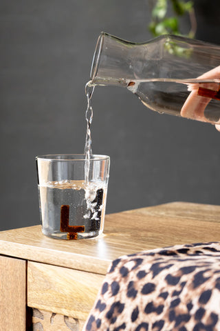 Glass being filled with water from a clear glass pitcher on a wooden surface.