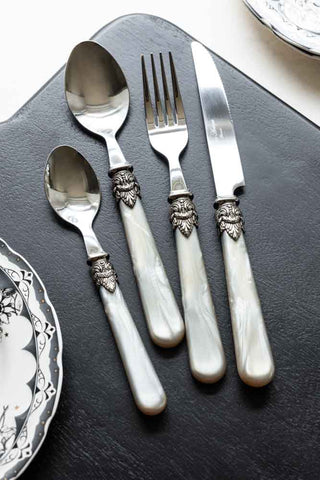 The Antique Champagne Cutlery 4-Piece Set displayed on a black chopping board on a white work surface, styled with two patterned plates.