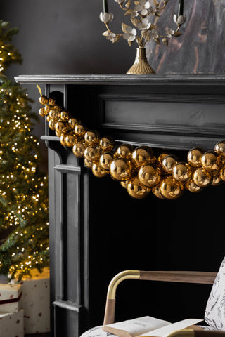Lifestyle image of the Antique-Effect Gold Bauble Christmas Garland on fireplace