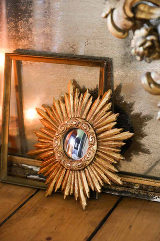Gold convex round mirror leaning against an aged portrait mirror