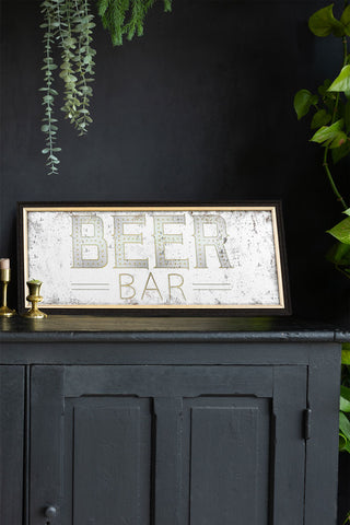 The Vintage-Style Beer Bar decorative Mirrored wall art displayed on a black sideboard, styled with some candlestick holders and various greenery.