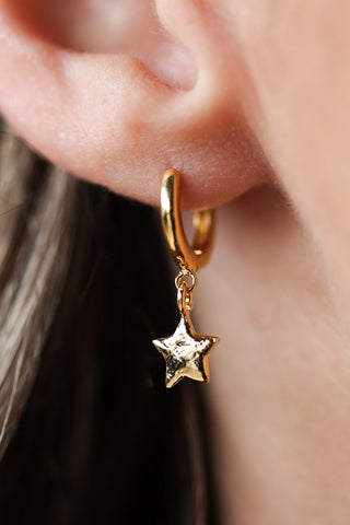 Lifestyle image of the You're A Star Gold Huggie Hoop Earrings on a model. 