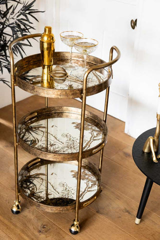 Gold bar cart with glass shelves on a wooden floor.