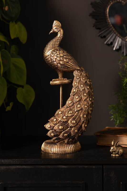 The Antique-Style Gold Peacock Ornament displayed on a dark sideboard with some greenery and other accessories.