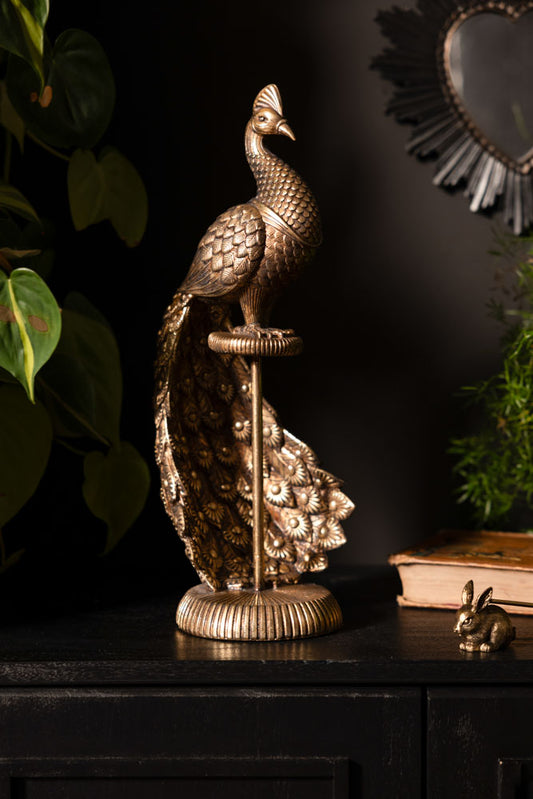 The Antique-Style Gold Peacock Ornament styled with other accessories and greenery, on a dark surface.