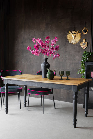 A styled image of the Apothecary Extendable Dining Table against a black wall with pink and black velvet chairs around it.