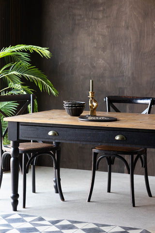 The Apothecary Dining Table styled with tableware, a candlestick holder, two chairs and a plant.