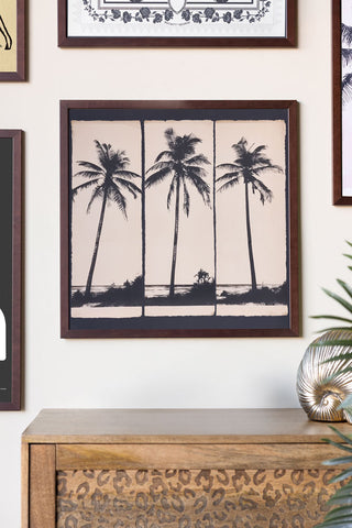 Framed artwork of palm trees on a wall above a wooden cabinet.