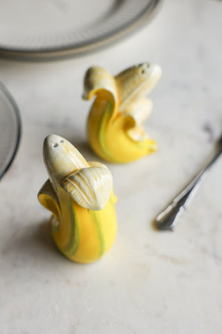 Banana Salt & Pepper Shakers displayed on a marble table with plates and cutlery.