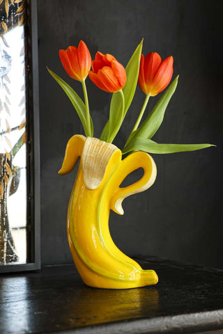 Lifestyle image of the Banana Vase styled on a black sideboard with tulips inside and a mirror in the background.