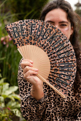 The Be Fucking Nice Leopard Print Fan being held by a model outdoors.