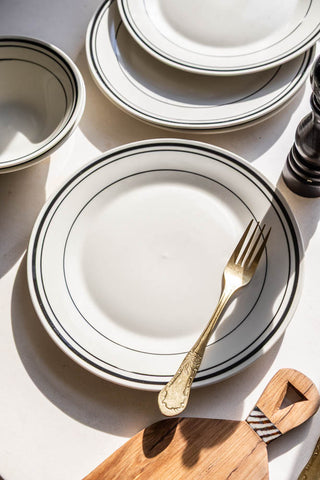 A lifestyle close up image of a bistro style black and white plate with a gold fork on it.