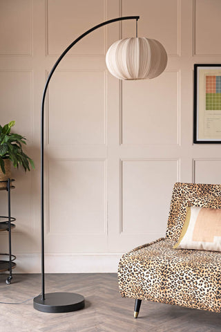 The Black Arch Floor Lamp with Neutral Pleated Fabric Lampshade styled next to a leopard print sofa in a living room.