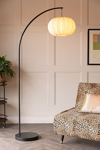The Black Arch Floor Lamp with Neutral Pleated Fabric Lampshade switched on and styled next to a leopard print sofa in a living room.