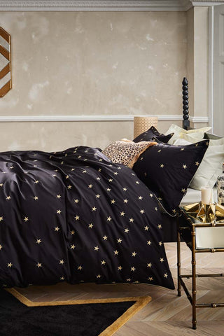 Lifestyle image of the Black Falling Star Duvet Cover and Pillow Case Set displayed on a bed and styled with various home accessories. 