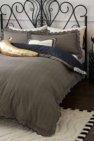The Black Pencil Stripe Scalloped Edge Bedding Set styled on a black metal bed.