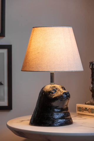 The Black Seal Table Lamp With Linen Shade switched on and displayed on a white marble table.