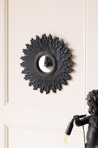 The Black Starburst Traditional Convex round Mirror on a wall above a lamp.