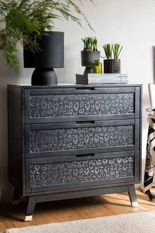 A lifestyle image of the Black Leopard Print Chest Of Drawers with plants and ornaments on it.